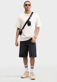 Afslappet outfit med en cremefarvet oversized t-shirt, sorte denimshorts, cremefarvede sneakers og stribet hvide strømper. Inkluderer en lille sort crossbody taske.