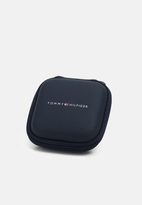 Tummansininen kovakotelo vetoketjulla, jossa on sileä pinta. Logo "TOMMY HILFIGER" on näkyvästi esillä edessä.