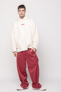 Oversized cremefarbener Hoodie mit "WARNING" Grafik, kombiniert mit locker sitzenden burgunderfarbenen Hosen. Weiße Sneaker runden das Outfit ab.