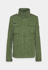 Grøn militærstil jakke lavet af tekstureret stof, med høj krave, to brystlommer og præget syning. Lynlås detaljer.