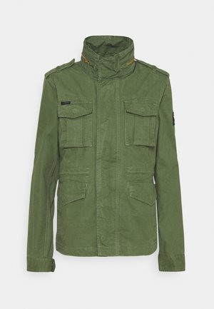 Grøn militærstil jakke lavet af tekstureret stof, med høj krave, to brystlommer og præget syning. Lynlås detaljer.