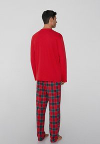 Top rojo de manga larga combinado con pantalones de pijama a cuadros en rojo, verde y azul. Tela suave con un corte holgado y diseño de pierna recta.