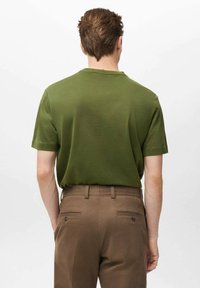Zelené tričko s krátkym rukávom vyrobené z bavlny, s okrúhlym výstrihom. Kombinované s hnedými nohavicami, ktoré majú zadné vrecká a gombíkové detaily.