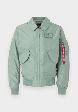 Hele rohelise bomber-tüüpi jakk esiluku, kahe kaldu taskuga, soonikkoes varrukaotste ja alumise servaga, rinnamärgiga ning punase „Remove Before Flight“ märgiga varrukal.