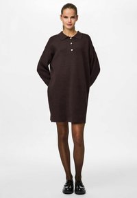 Vestido marrón a la altura de la rodilla en tejido suave, con cuello y tres botones. Corte holgado y mangas largas con aberturas con puños.