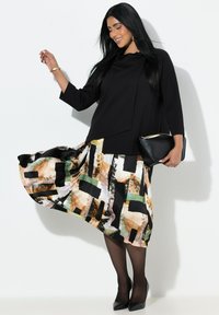 Zwart langärmelig top met gedrapeerde halslijn, gecombineerd met een contrasterende, patroonrijke rok met abstracte kleuren en vormen, zwarte hakken en een zwarte clutch.