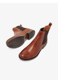 Botas Chelsea de cuero marrón con paneles laterales elásticos, punta redonda y suela de goma texturizada. Cuenta con una cinta en la parte trasera para ponerlas y quitarlas fácilmente.