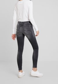 Cienkie dżinsy w wyblakłym czarnym dennie z gładką teksturą. Posiadają dwie tylne kieszenie i średnią talię, zestawione z białymi sneakersami.