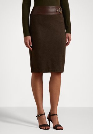 Femme portant une jupe crayon brun foncé longueur genou avec une ceinture en cuir marron avec boucle et des sandales noires à talons hauts avec bride à la cheville, debout.