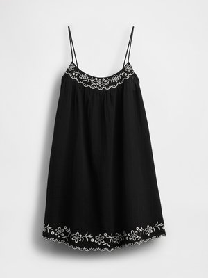 Mustamudi õhukeste rihmadega kleit, millel on lilleline valge tikand kaeluses ja hemides, tavalise valge tausta taustal.