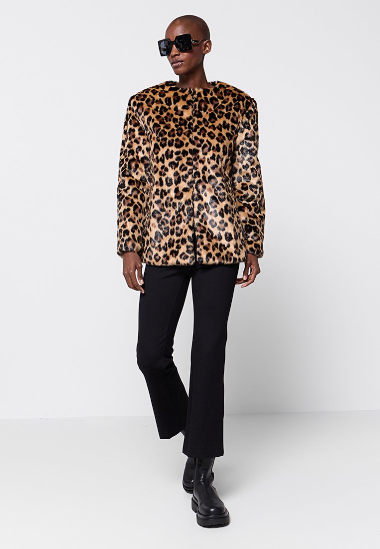 Abrigo de piel sintética de leopardo con una silueta recta, hombros redondeados y cierre de botón. Combinado con pantalones negros y botas gruesas.