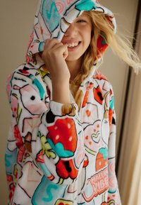 Tuta intera in pile con cappuccio, caratterizzata da un motivo colorato di frutti, forme e disegni giocosi su sfondo bianco. Tessuto morbido su tutta la superficie.