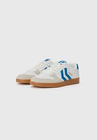 White sneakers with blue accents and tan suede detailing, featuring a classic lace-up design and a rubber gum sole.