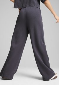 Pantaloni a gamba larga in tessuto grigio scuro, con una morbida trama e una vita elastica, abbinati a un top corto per comfort e facilità di movimento.