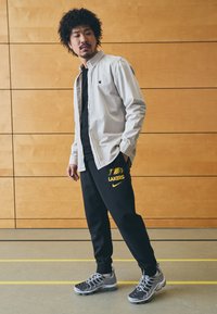 Lys grå skjorte med knapper over en svart t-skjorte, kombinert med svarte joggebukser med gult "LAKERS" logo, og grå joggesko.