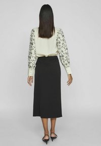 Zwarte mid-length rok met elastische tailleband, gecombineerd met een lichte crèmekleurige blouse met zwarte bloemenborduursels op de lange mouwen.