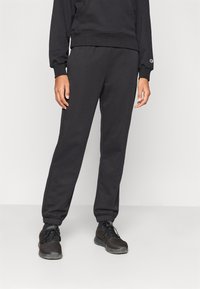 Μαύρο, φούτερ παντελόνι από βαμβακερό μείγμα με ελαστική μέση και μανσέτες. Διαθέτει πλαϊνές τσέπες και άνετη εφαρμογή. Φοριέται με ταιριαστά μαύρα αθλητικά παπούτσια.