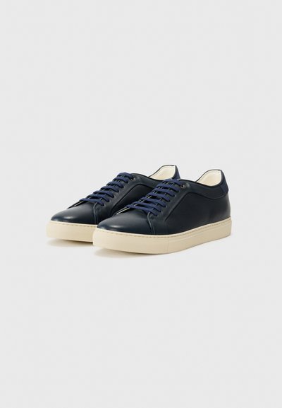 Ténis de couro azul-marinho com bico arredondado, parte superior texturizada e sola de borracha creme em contraste. Apresenta atacadores planos azul-marinho e detalhes de costura.