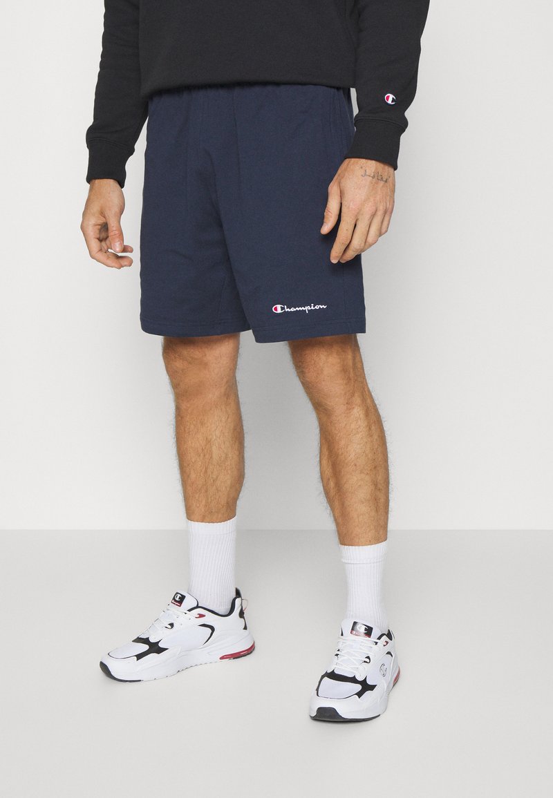 Pantalones cortos de deporte en azul marino con cintura elástica y pequeño logotipo de "Champion" bordado en blanco y rojo en el lado izquierdo.