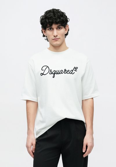 White cotton t-shirt with short sleeves, featuring a black cursive "Dsquared²" logo across the chest, paired with black trousers.