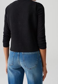 Černý zkrácený svetr s dlouhými rukávy a texturovanou tkaninou, spárovaný se světle modrými džíny s vysokým pasem a zadními kapsami a se světle vybledlým vzhledem.