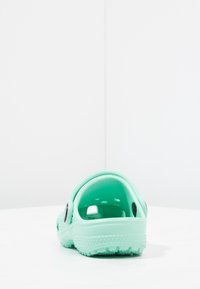 Mintegroene rubberen klompen met een gestructureerde zool en een open achterkant, voorzien van gaten aan de zijkanten voor ventilatie en een ronde accent.