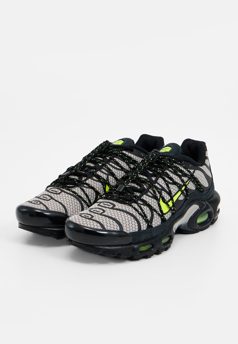 Sneakers a rete grigie con accenti neri e dettagli verde fluo. Presentano una tomaia testurizzata e pod d'aria a cuscinetto visibili sulla suola.