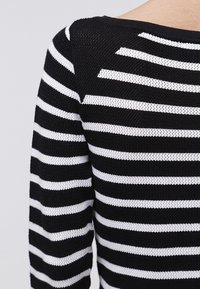 Schwarz-weiß gestreifter Strickpullover mit strukturierter Oberfläche, der horizontale Streifen und einen weiten Halsausschnitt aufweist.