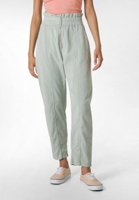 Lichtgroene, taps toelopende broek met elastische tailleband en een ritssluiting aan de voorkant. Bevat zijnaad- en kniezijde-details. Gepaard met beige sneakers.