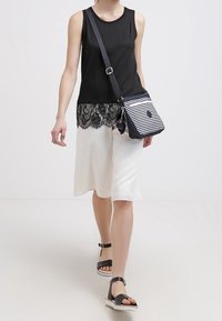 Top nero senza maniche con orlo in pizzo, pantaloni corti bianchi a gamba larga e sandali neri. È inclusa una borsa a tracolla a righe con un charm.
