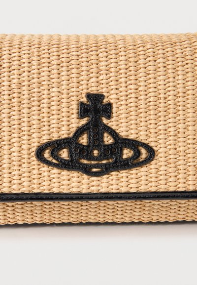 Υφαντό μπεζ τσαντάκι χειρός με μαύρο υφασμάτινο έμβλημα σε σχήμα σφαίρας που χαρακτηρίζεται από ένα σταυρό στην κορυφή, τοποθετημένο στο κέντρο πάνω από μια μαύρη ταινία.
