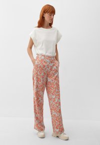 T-shirt bianco, a maniche corte e dal taglio boxy, abbinato a pantaloni larghi arancioni con motivo floreale, caratterizzati da dettagli blu e tasche laterali.