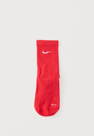Czerwona sportowa skarpeta Nike z białym logo Swoosh blisko góry i oznaczeniami rozmiaru na palcach, położona płasko na białym tle.