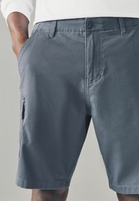 Pantaloni scurți gri din bumbac, cu fața plată, buzunare laterale și un singur buzunar cargo, având sistem de închidere cu buton și margine dreaptă.