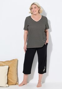 Camiseta de cuello en V a rayas en negro y beige, combinada con pantalones capri negros que cuentan con un bordado decorativo de plumas en el dobladillo.