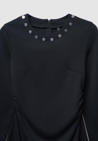 Schwarzes Kleid mit rundem Ausschnitt, verziert mit silbernen metallischen Nieten entlang des Kragens und Raffung an der Seite. Mit Reißverschluss auf der Rückseite.