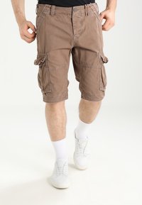 Pantalones cortos de carga marrones con múltiples bolsillos, diseño recto, fabricados con un tejido duradero, combinados con calcetines y zapatos blancos.