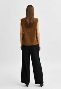 Haut sans manches marron avec une finition texturée, associé à un pantalon ample noir et des chaussures à talons. Design simple, sans motifs ni accents visibles.