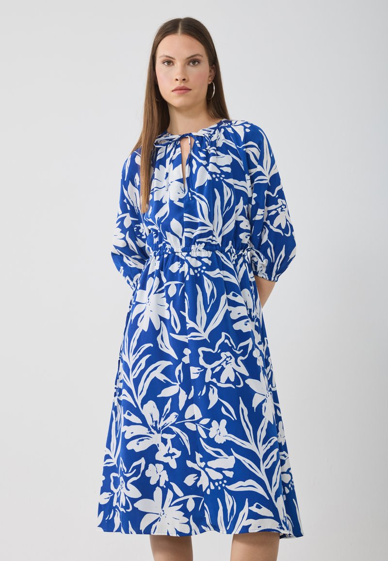 Robe floral bleue avec des motifs blancs, ceinture à la taille, col rond et manches trois-quarts. Tissu léger avec une coupe ample.