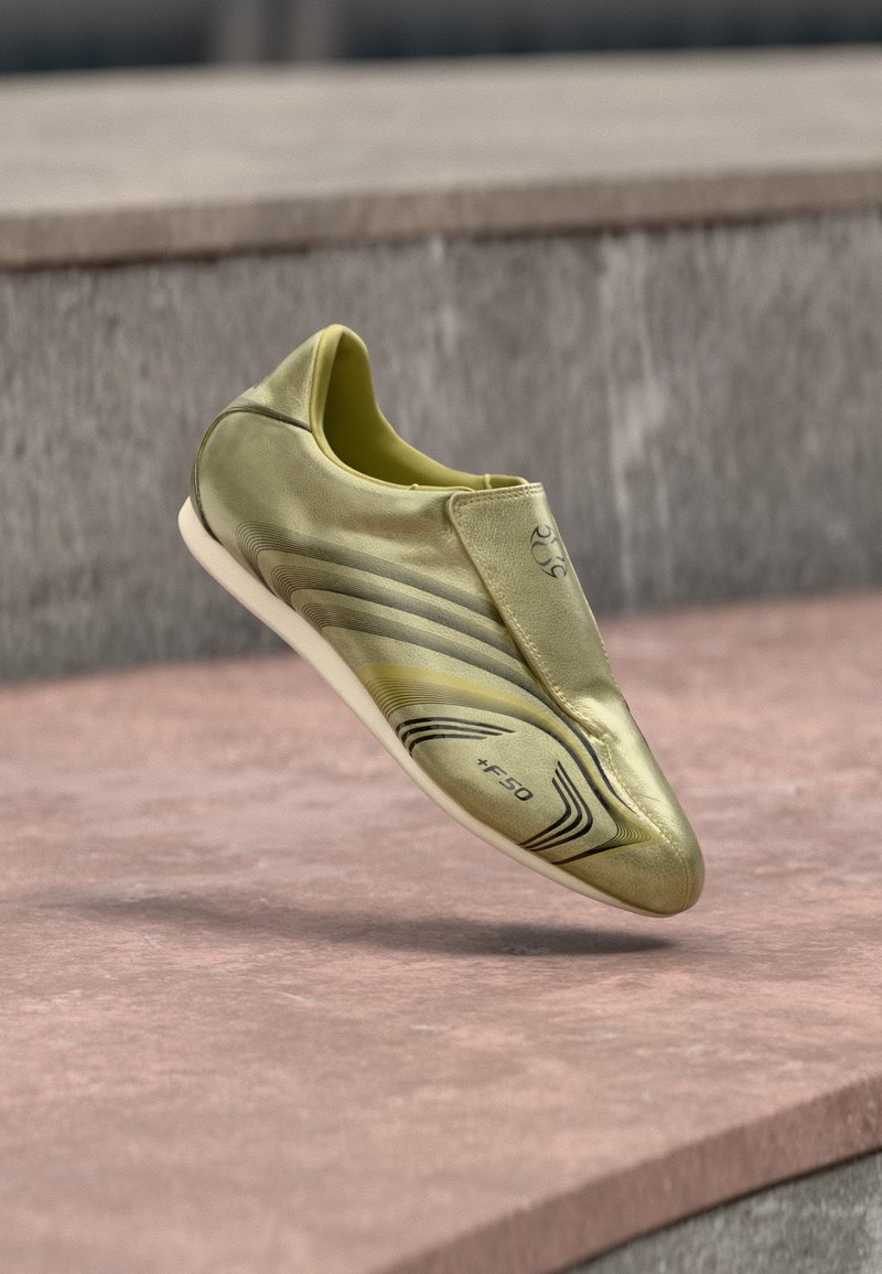 Kuldne jalgpallijalats elegantse disainiga, sileda sünteetilise materjaliga, libisemisvaba stiiliga ja mustade joontega, millel on "+F50" logo.