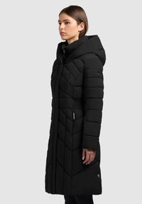 Zwarte geïsoleerde pufferjas met een doorgestikt ontwerp, hoge kraag, ritssluiting, capuchon en zijzakken. Getailleerde pasvorm met elastische accenten.