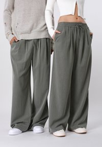 Szürke csíkos, bő szárú nadrág gumis derékrésszel, fehér és bézs kényelmes cipővel párosítva. Texturált anyag mély oldalzsebekkel.