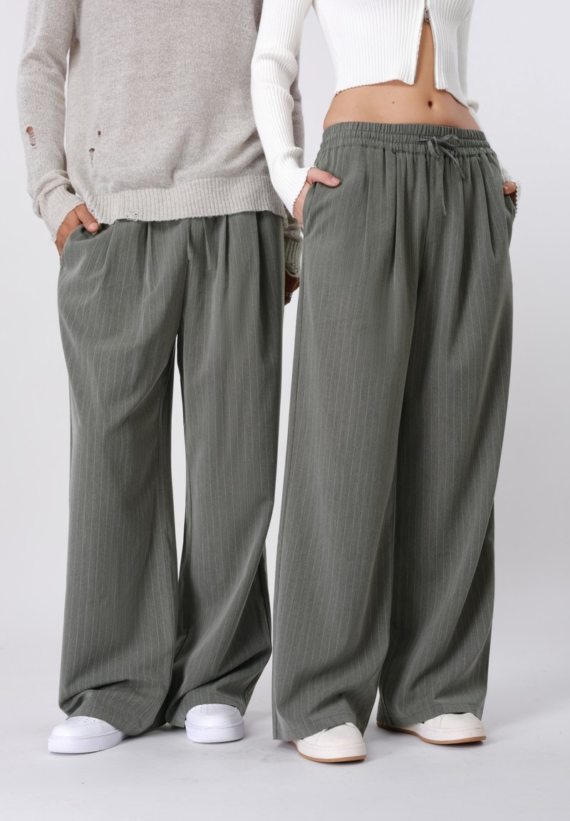 Szürke csíkos, bő szárú nadrág gumis derékrésszel, fehér és bézs kényelmes cipővel párosítva. Texturált anyag mély oldalzsebekkel.