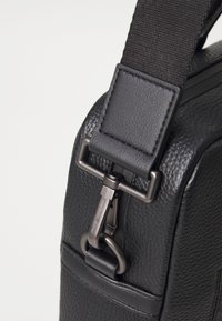 Black textured leather bag with a durable fabric strap and a metal clip closure. Features a smooth finish and subtle stitching details.