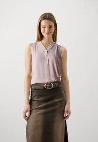 Top senza maniche di un rosa chiaro con scollatura a V e bottoni, abbinato a una gonna marrone con una grande fibbia rotonda. Texture liscia.