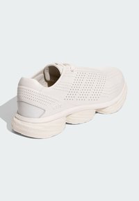 Chaussure de sport blanche avec une tige perforée, une semelle arrondie avec des détails texturés et un design arrière distinctif.