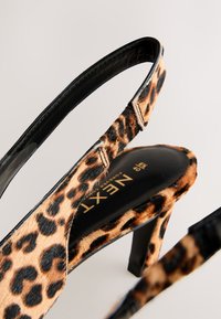 Chaussure à talon haut à bride arrière imprimé léopard avec semelle intérieure noire et nom de marque partiellement visible "NEXT" sur la semelle.