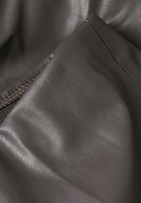 Braunes Ledergewebe mit einer glatten Textur, sichtbarer Naht und einem Reißverschlussdetails an einer Kante.