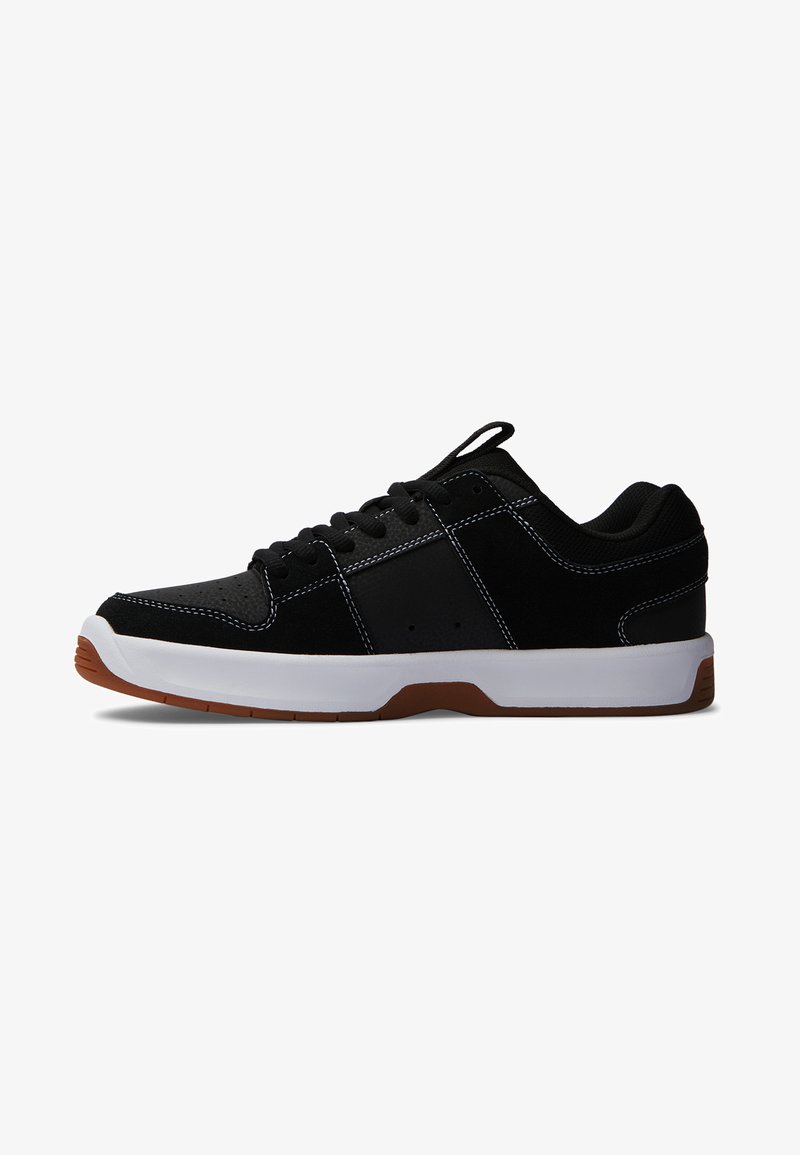 Black athletic sneaker with a suede and mesh upper, white midsole, and brown rubber outsole. Features contrasting white stitching and lace-up design.