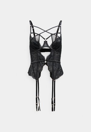 Zwarte kanten korset met doorschijnende mesh cups, kruislingse banden, golvende randen, verstelbare kousenbanden en accenten in goudkleurige hardware.